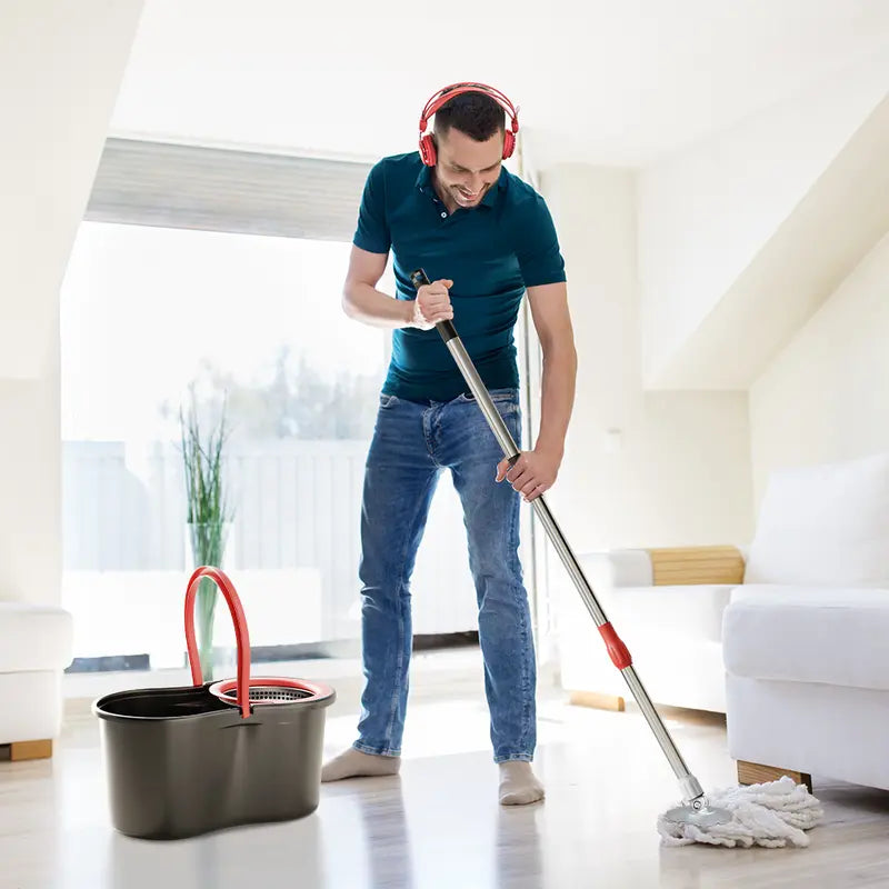 Man cleaning a floor with a mop and bucket in a bright living room.
